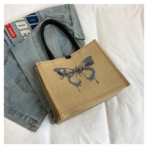 Close-up of beige linen tote bag featuring dark blue butterfly print and black handles
