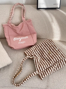 Pink canvas Bonjour tote bag and brown striped faux fur shoulder bag on a beige sofa