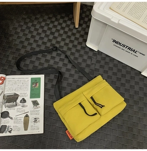 Yellow nylon sacoche bag with dual pockets on a textured mat with camping magazines