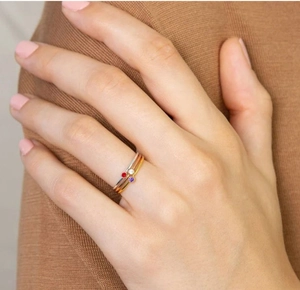 Primer plano de tres anillos finos de oro con piedras de colores apilados en una mano