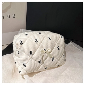 Detailed view of white quilted cotton makeup bag with black bow embroidery and bow detail