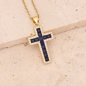 Macro shot of gold cross pendant with dark blue sapphire-style gems and white cubic zirconia
