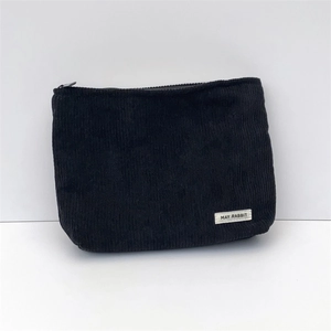 Macro detail of black corduroy makeup bag with MAY RABBIT label on white background