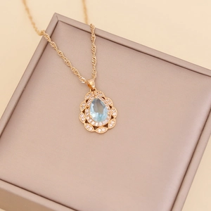 Detail of gold water drop necklace with light blue gemstone and white zircon accents