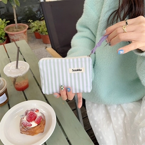 Close-up of small striped lipstick pouch with purple zipper and wristlet strap
