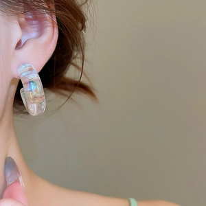 Close-up of model wearing iridescent acrylic C-shape hoop earrings with colorful gloss