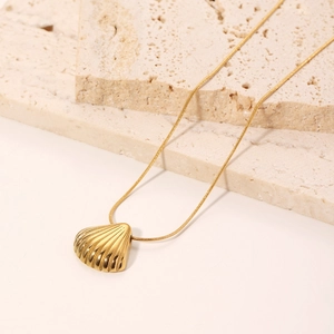 Minimalist gold shell pendant necklace with snake chain on natural stone background