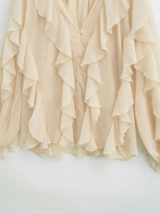 Detail of beige V-neck blouse featuring elegant layered ruffles and chiffon fabric