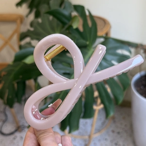 Pale pink glossy oversized hair claw clip held by hand in a minimalist home setting