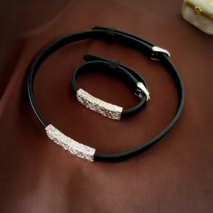 Detail of black leather necklace and bracelet set with engraved silver metal buckles
