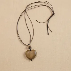 Vintage style heart-shaped wooden pendant necklace with brown cord on a tray