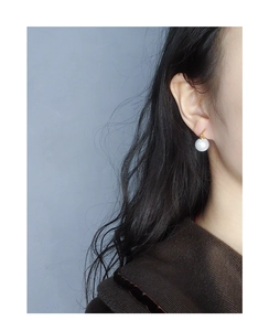 Close-up of a high-quality white round pearl earring worn on ear with golden hook