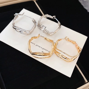 Close-up of layered irregular wavy metal hoop earrings in gold and silver finishes