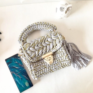 Detail view of a handmade grey crochet crossbody bag with golden metallic lock and tassel