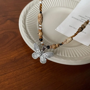Detail of beaded necklace with silver butterfly pendant and brown stones on ceramic