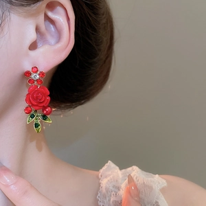 Close-up of elegant red rose earrings with sparkling crystals and green leaf details