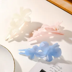 Detailed view of three glossy butterfly hair clips in cream, pink, and sky blue colors