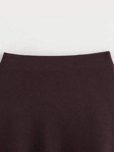 Close-up detail of dark brown knit vest fabric texture and finely stitched hem edges