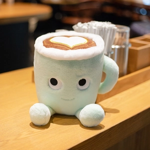 Cute latte coffee cup plush toy with green body and heart latte art on blurred cafe background
