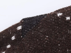 Macro view of dark brown knitted fabric with white spots showing detailed fiber texture