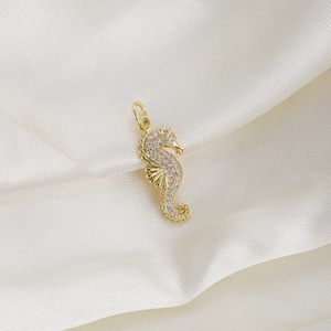 Detailed view of a golden seahorse pendant inlaid with sparkling zircons on white silk