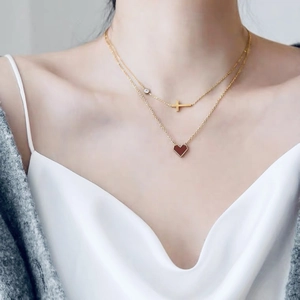 Close-up of layered gold necklace featuring a red heart pendant and tiny cross detail