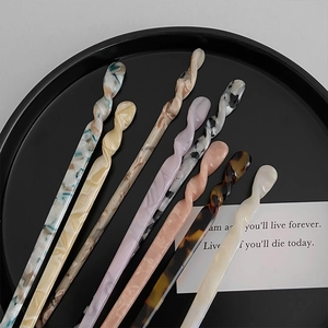 Macro shot of assorted colorful marble-patterned acetate hair pins in a black tray