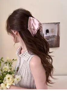 Détail de la pince à cheveux en satin rose avec bouton doré sur longs cheveux ondulés
