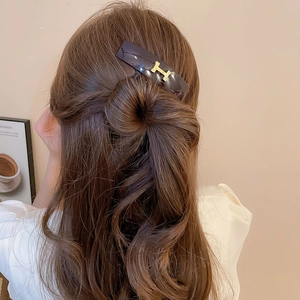 Detailed view of a tortoiseshell hair clip with a gold H-letter logo on half-tied hair