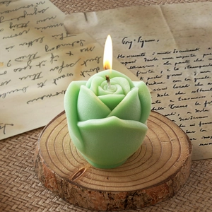 Detailed view of mint green 3D rose candle with flame on rustic wooden base stand
