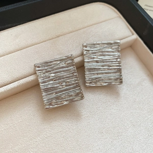Detailed close-up of silver rectangular stud earrings with a textured metallic finish