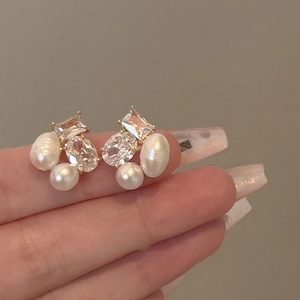 Detailed close-up of gold stud earrings with baroque pearls and clear zircon stones