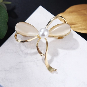 Elegant gold bow brooch with pearl and opal elements on white marble platform