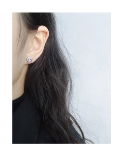 Close-up of heart-shaped purple zircon stud earring on ear with silver finish
