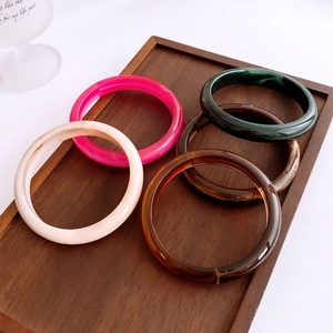 Minimalist vintage acrylic resin bangles in multiple colors on a dark wooden tray