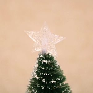 Close-up of mini snow-flocked desktop Christmas tree with a transparent frosted star topper