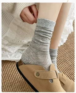 Detail of grey knitted mid-tube socks paired with khaki suede mules on a woven rug
