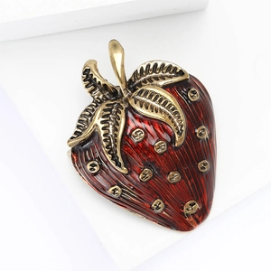 Vintage red enamel strawberry brooch with golden metallic accents on a white display stand