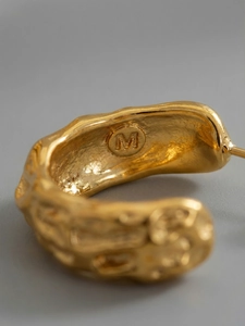 Macro shot of polished gold C-shape earrings with unique irregular texture and M stamp