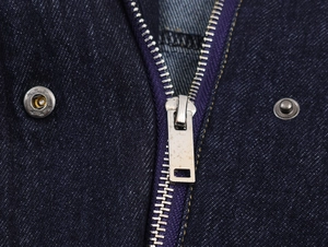 Vue détaillée du tissu denim bleu foncé avec fermeture éclair argentée et bouton métallique
