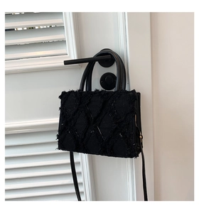 Close-up of black quilted tweed texture with fringed edges and metallic accents on handbag