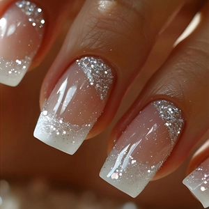 Makroaufnahme von French-Ombre-Kunstnägeln mit glitzerndem Silberstaub und weißen Spitzen