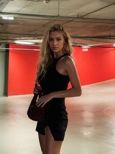 Sleeveless black slit mini dress paired with a burgundy woven handbag in a garage