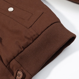 Detail of brown parka jacket showing ribbed cuffs, twill fabric, and metal button closure