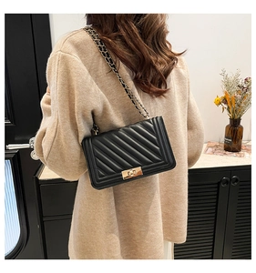 Detail of a quilted black leather shoulder bag with gold chain strap and metal lock clasp