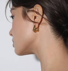Close-up of a model wearing golden irregular lava fold earrings with a metallic texture
