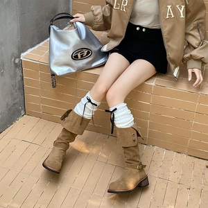 Detail of white knitted leg warmers with black bow knots over brown suede boots