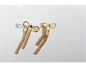 Detail of gold bow earrings with cascading white rhinestone tassels on a white background