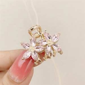 Pink crystal flower hair claw clip with golden metal finish held by hand on beige background