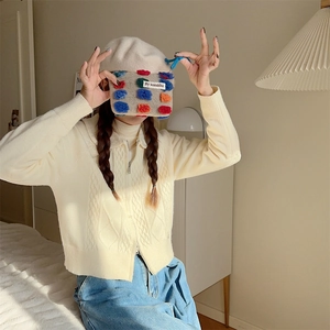 Dettaglio della borsa per cosmetici in maglia crema con pompon colorati e logo